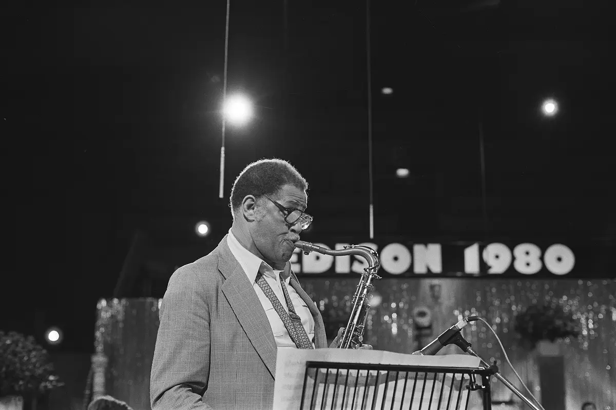 Dexter Gordon plays tenor saxophone at a music stand, a lit sign behind him