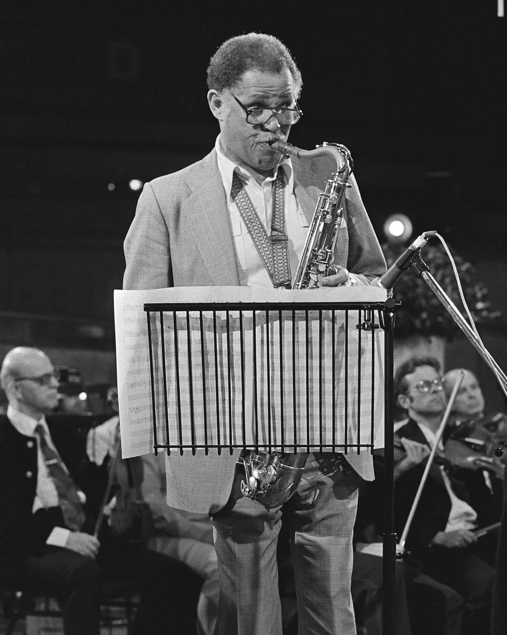 Dexter Gordon plays tenor saxophone standing behind a music stand, the orchestra seated behind him